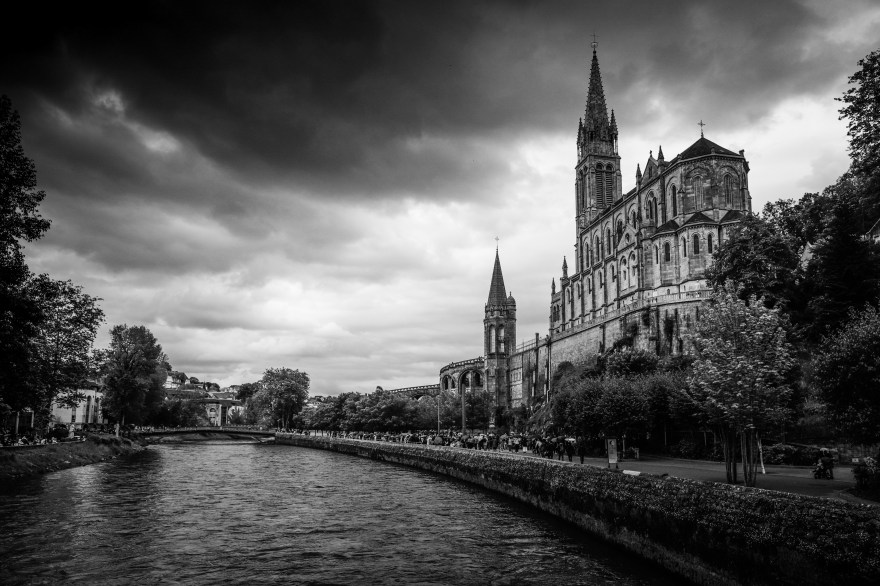 The Basilica of Our Lady of the Immaculate Conception in Lourdes, captured in black and white—clouds gathering, light slipping across stone and river. One of many stories still to come.